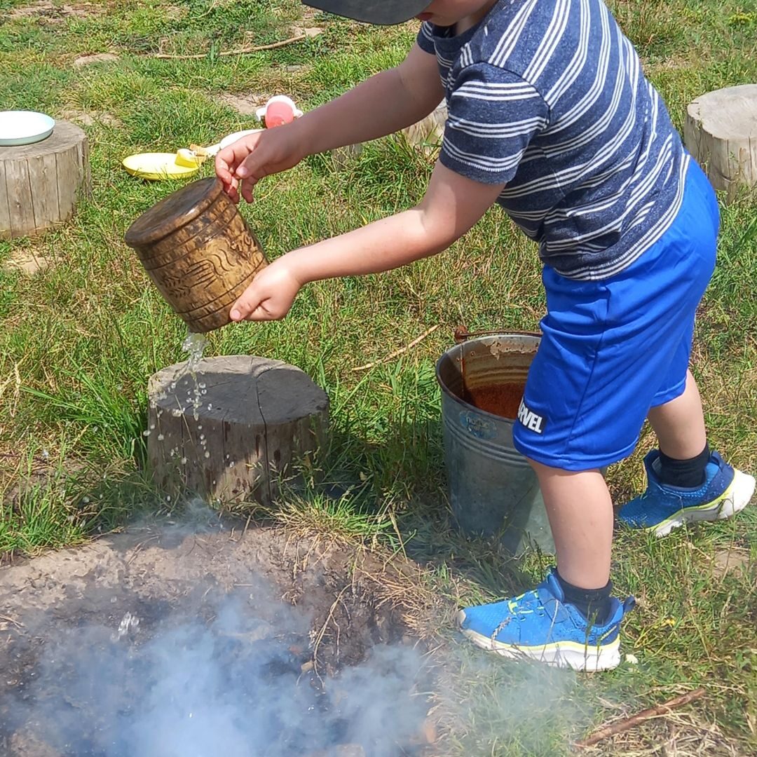 A child pouring water at a tree-stump table