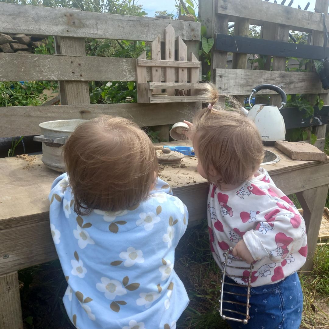 Two children playing at the mud kitchen bench