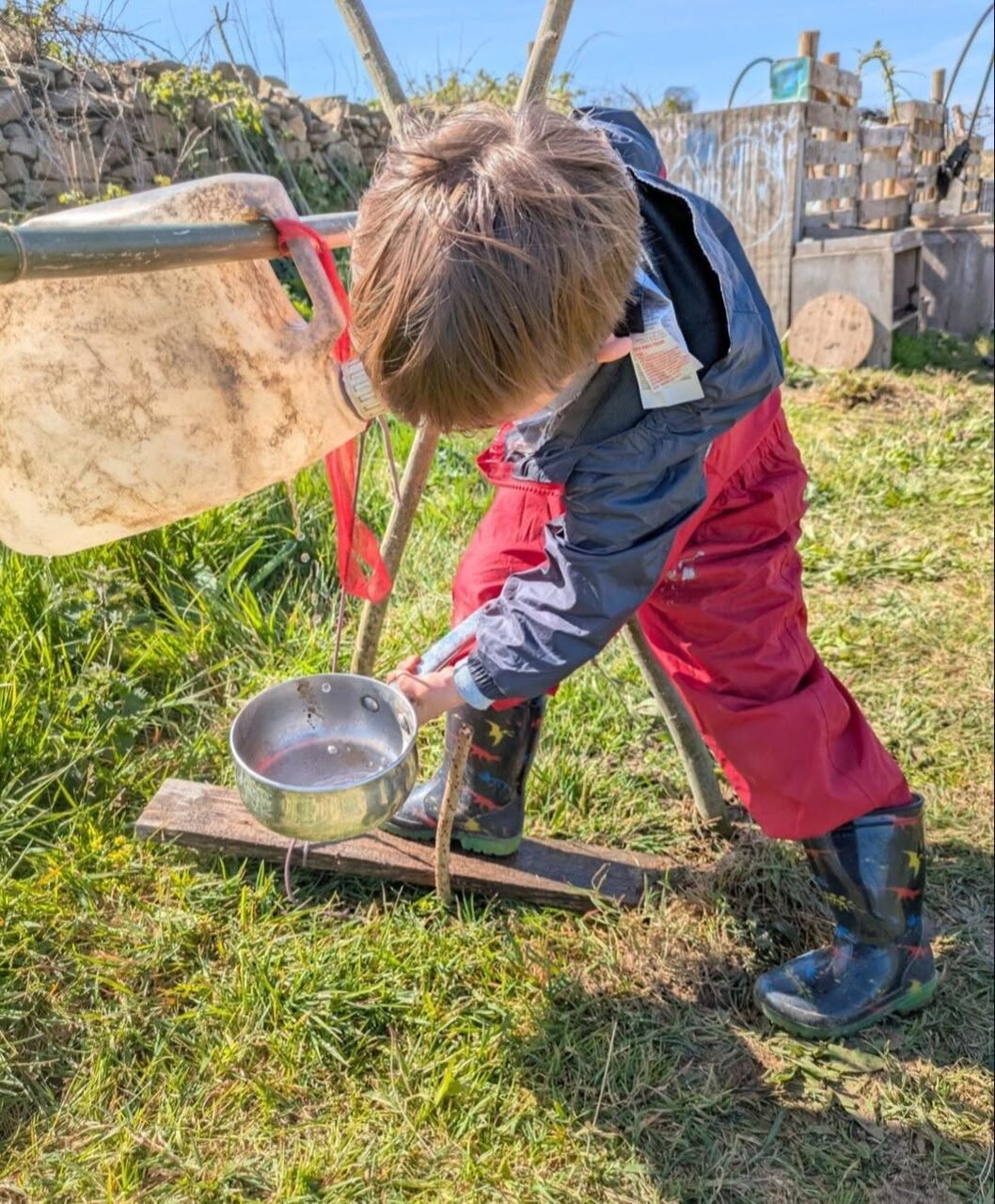 A child pouring water at the mud kitchen